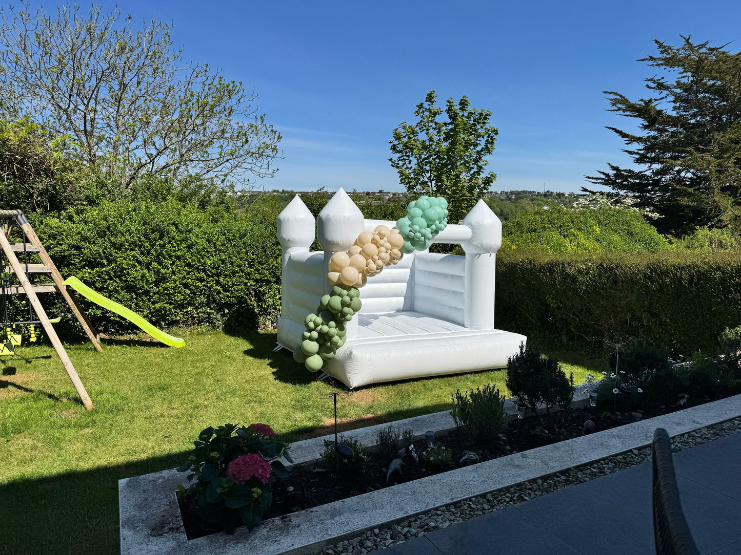 White Bouncy Castle with Custom Green & Gold Balloon Garland in a Back Garden