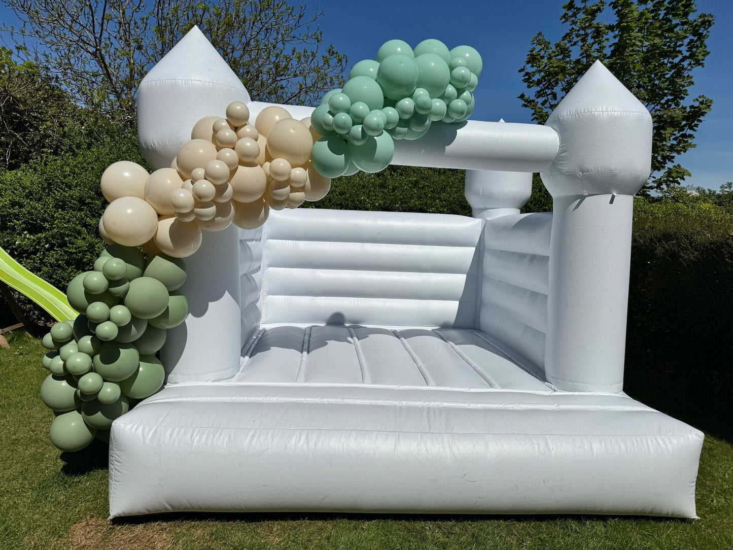 White Bouncy Castle with Custom Green & Gold Balloon Garland in a Back Garden, Cork