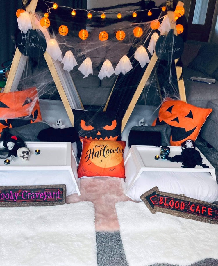 A Halloween themed teepee setup with decorations including pumpkin faces, spider webs, and Halloween accessories displayed on the floor inside the teepee.